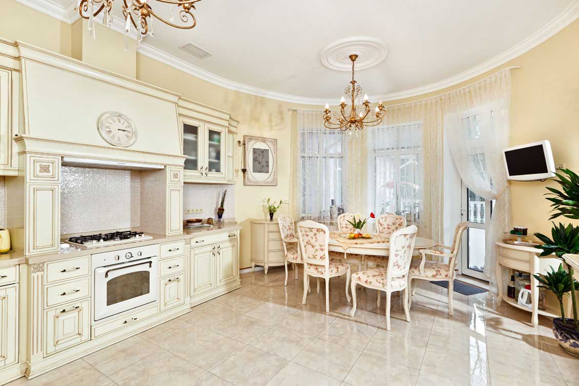 Luksusowa, ekskluzywna drewniana kuchnia na wymiar otwarta na salon. Meble kuchenne w kolorze białym, ponadto elegancki drewniany stół i krzesła.