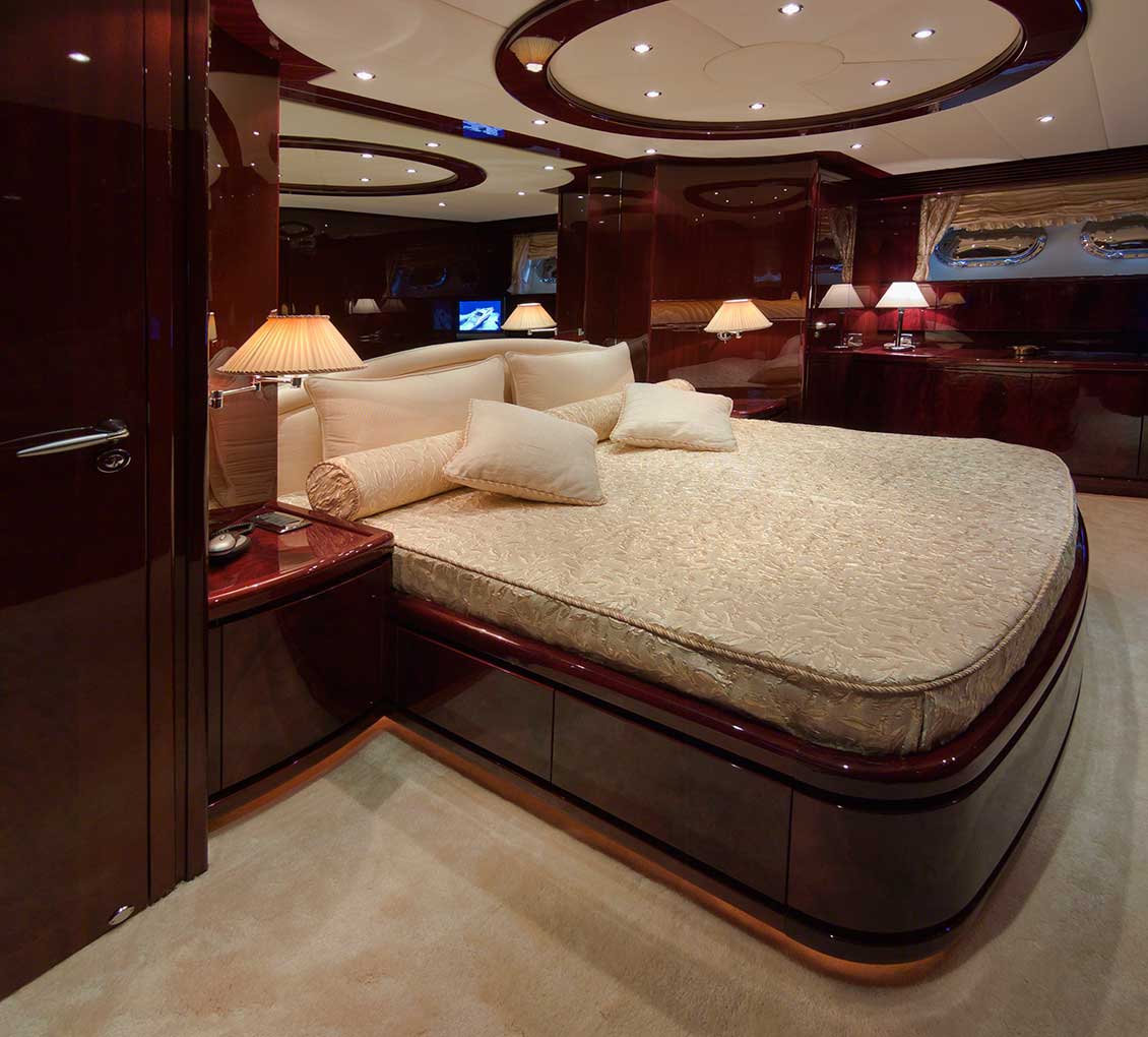 Ekskluzywne meble na wymiar we wnętrzu niezwykle luksusowego jachtu. Meble drewniane na zamówienie lśniące nowością i prestiżem; na pierwszym planie duże, komfortowe łóżko..
