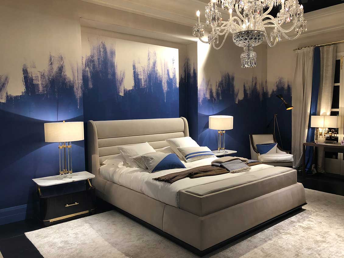 Spore dwuosobowe łóżko w pokoju domu studenckiego. Łóżko białe (choć poduszki mają niebieskie akcenty), a ściany biało - niebieskie