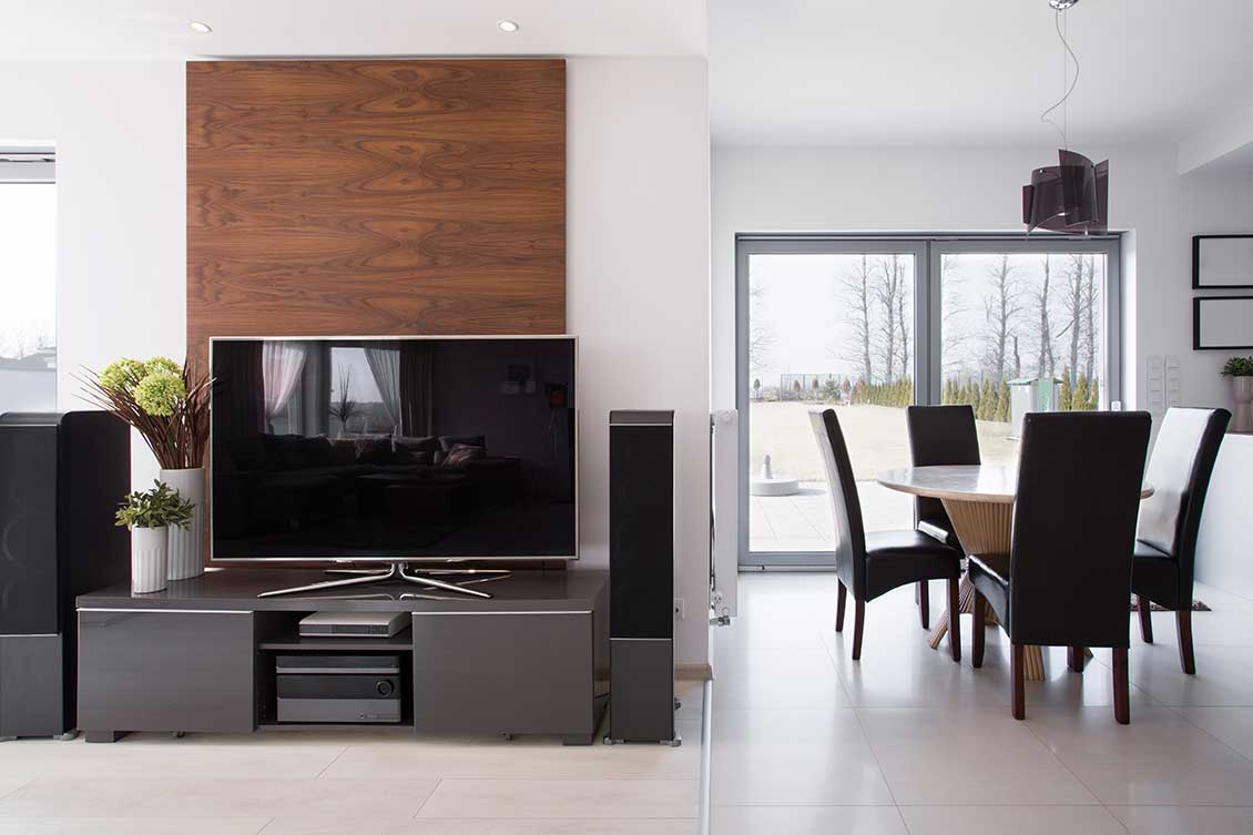 Nowoczesne wyposażenie i meble do apartamentów: stolik RTV z telewizorem, za nim drewniane panele ścienne, na prawo stół i krzesła