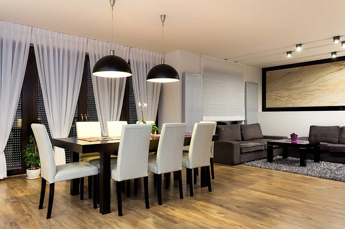 Nowoczesne, eleganckie meble do apartamentów, meble na wymiar: na pierwszym planie duży czarny, drewniany stół i czarno-białe krzesła, dalej dwie brązowe sofy i czarny stolik